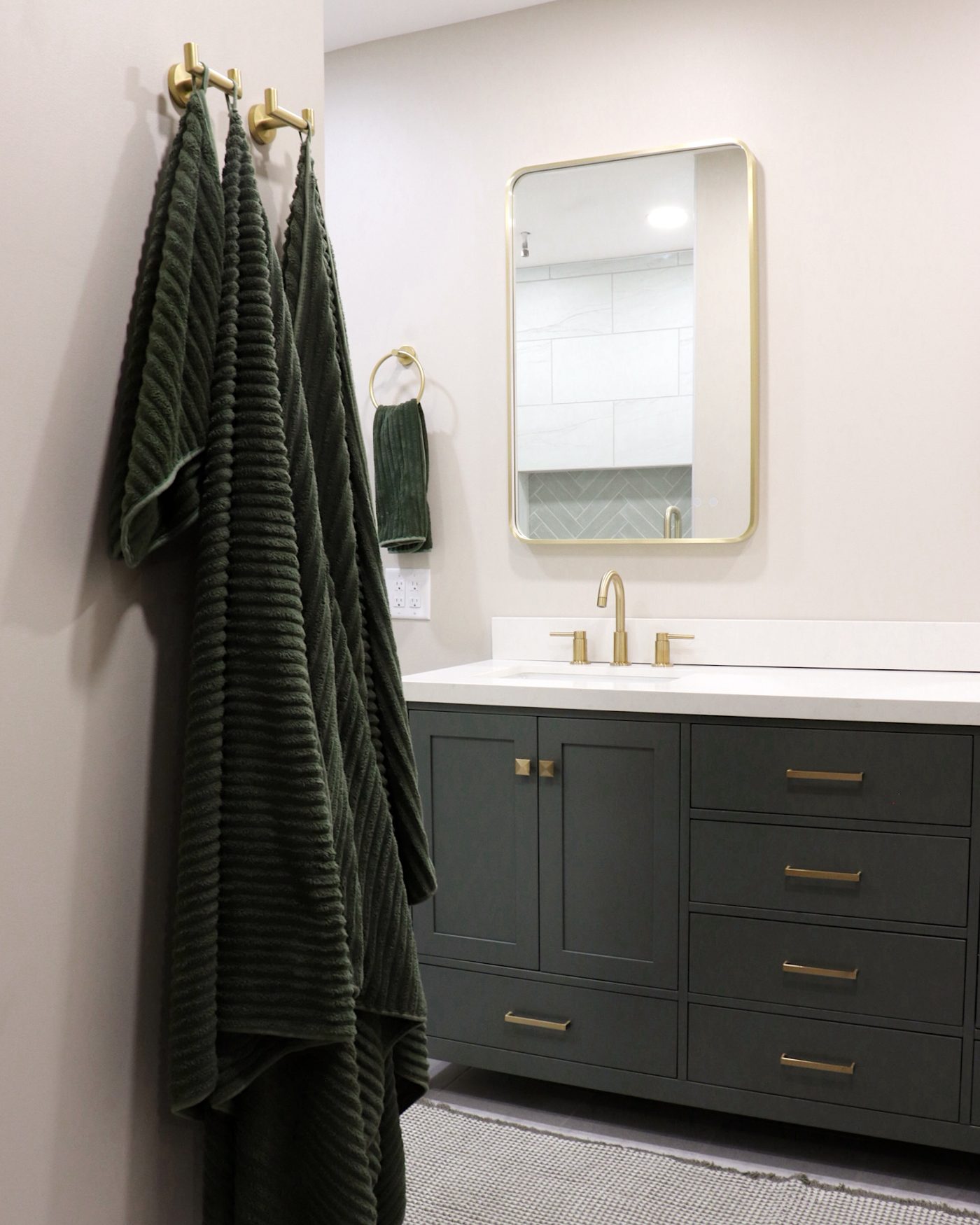 Dark green bathroom vanity with brass fixtures, part of a bathroom remodel by NK Construction